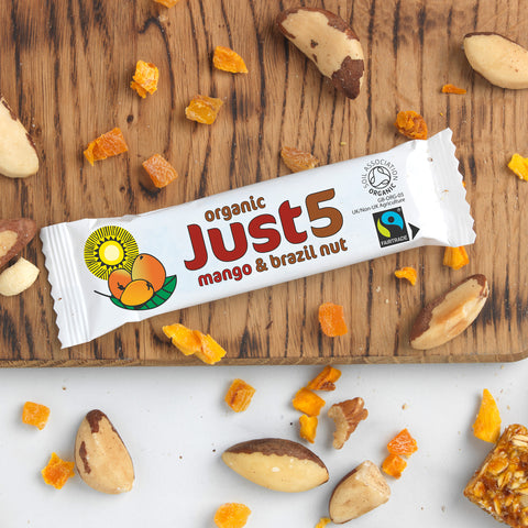 front of organic Just 5 mango and brazil nut bar on table top with brazil nuts and dried mango pieces scattered