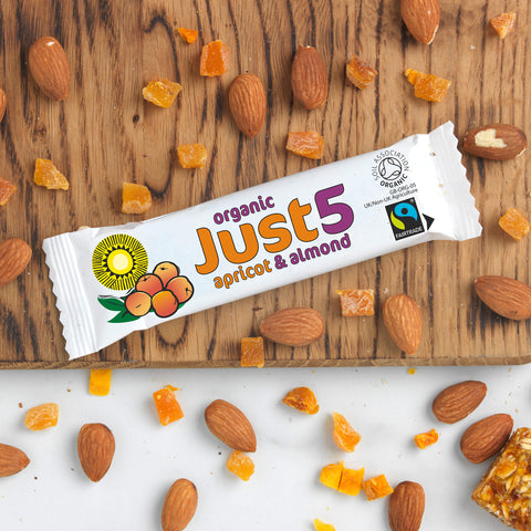 front of organic Just 5 apricot and almond bar on table top with almonds and dried apricot pieces scattered